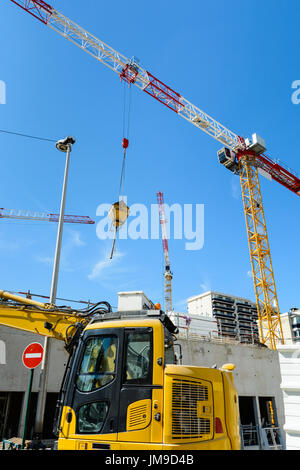 Niedrigen Winkel Ansicht von Turmdrehkranen auf einer Baustelle mit gelben Bagger im Vordergrund. Stockfoto