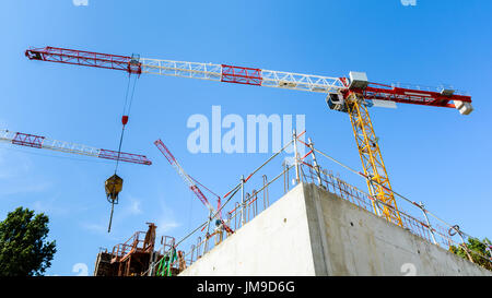 Niedrigen Sie Winkel Ansicht von drei Turmdrehkranen auf einer Baustelle mit einem Betongebäude im Bau in den Vordergrund und blauer Himmel. Stockfoto