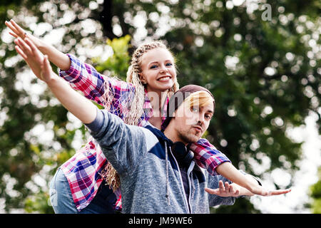 Junges Paar außergewöhnliche herumtollen in der Sommerpark. Der Kerl trägt Freundin auf dem Rücken. Stockfoto