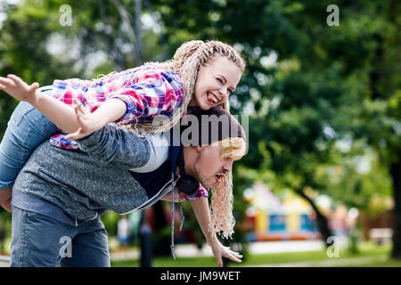 Junges Paar außergewöhnliche herumtollen in der Sommerpark. Der Kerl trägt Freundin auf dem Rücken. Stockfoto