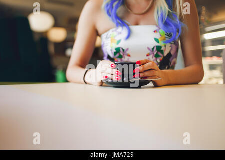 Kaffeebecher in der hand, eine rote Maniküre. Trendige Mädchen mit leuchtend gefärbten Haaren, im Café sitzen. Stockfoto