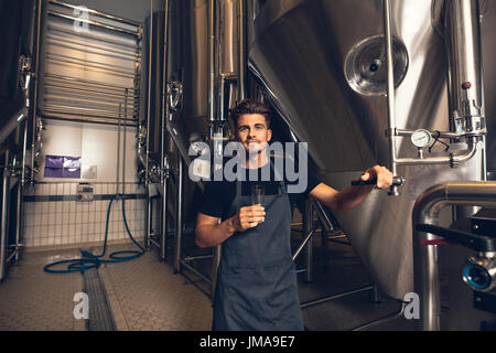 Porträt von männlichen Brewer von Tank in Brauerei stehen. Mann das Bier bei der Verarbeitung von Abschnitt untersucht. Stockfoto