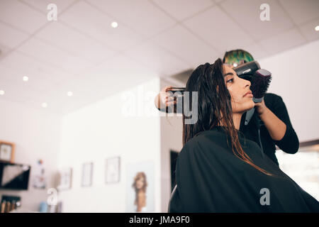 Weibliche Friseur mit Gebläse und Pinsel, um trockenes Haar. Frau an eine anspruchsvolle Schönheitssalon immer eine Frisur. Stockfoto