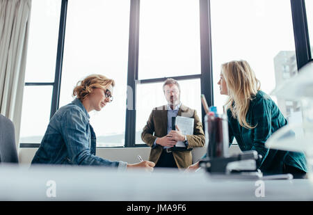 Geschäftsleute in modernen Büro. Geschäftsfrau sitzt an ihrem Schreibtisch mit Kollegen stehen. Stockfoto
