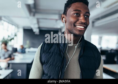 Männliche Führungskraft anhören von Musik mit Kopfhörern während Sie im Büro stehen. Afrikanische junge Mann Musik hören im Konstruktionsbüro. Stockfoto