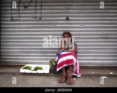 ANTIPOLO CITY, Philippinen - 19. Juli 2017: Eine Frau verkauft Gemüse auf einem Bürgersteig entlang einer Straße in Antipolo City. Stockfoto