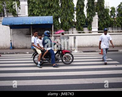 ANTIPOLO CITY, Philippinen - 19. Juli 2017: Ein Motorradfahrer mit zwei Passagiere stoppt, einen Mann auf einem Fußgängerweg passieren zu lassen. Stockfoto
