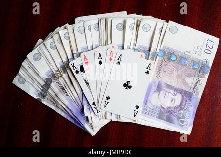 Vier Asse und ein König, eine glückliche gewinnende Pokerhand und ein Vermögen in 20 Pfund-Noten auf einem dunklen Tisch Stockfoto