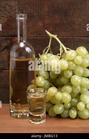 Geöffnete Flasche Grappa in der Nähe von Weinglas und Weintraube vor alten hölzernen Hintergrund Stockfoto