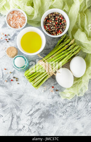 Bündel von rohen Spargel, Salz, Pfeffer, Olivenöl und frischen Eiern auf hellem Hintergrund. Ansicht von oben Stockfoto