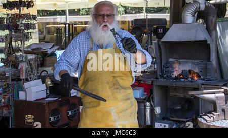 Cetinje, Montenegro - gealterte Schmied, Horseshoe Souvenirs und unterhaltsame Touristen in einer Straße workshop Stockfoto