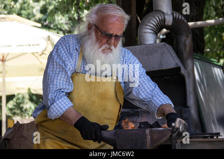 Cetinje, Montenegro - gealterte Schmied, Horseshoe Souvenirs und unterhaltsame Touristen in einer Straße workshop Stockfoto