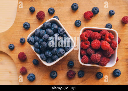Heidelbeeren und Himbeeren in weiße Keramikschale auf Holztisch Stockfoto