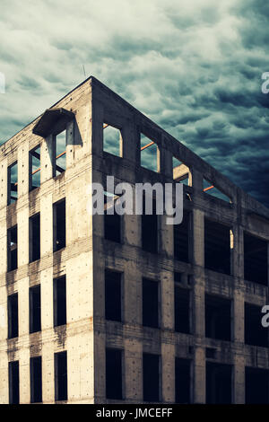 Verlassene konkrete Rohbau Fassade mit stürmischen Wolken im Hintergrund Stockfoto