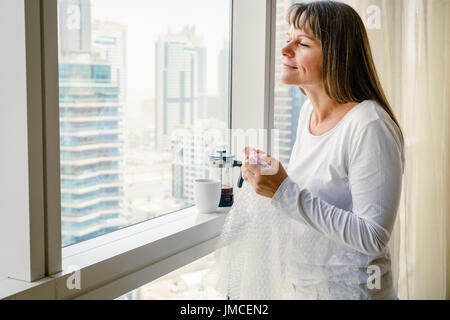 Reife Frau am Fenster ist Stress die Freigabe durch knallende Luftpolsterfolie Stockfoto