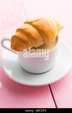 Süße leckere Croissants und Kaffeetasse auf rosa Tisch. Stockfoto