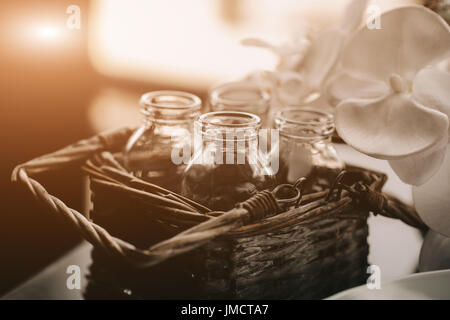 Glas Flasche in vintage Weidenkorb. Einrichtung im Loft Interieur. Blume blackground verwischt. Vintage toning Foto. Flare für Design und rext. Stockfoto