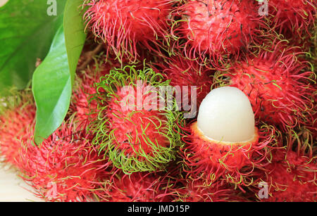 Reihe von leuchtenden Farben reif Rambutan ganze Früchte und geöffnet, um köstliches saftiges weißes Fleisch zeigen Stockfoto