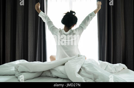 Asiatische Frauen aufwachen aus dem Schlaf. sind dehnen sich in der früh am Wochenende sitzen auf dem Bett im Luxus-Zimmer in Relax und Wochenende-Konzept Stockfoto