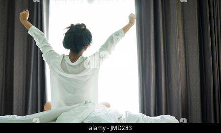 Asiatische Frauen aufwachen aus dem Schlaf. sind dehnen sich in der früh am Wochenende sitzen auf dem Bett im Luxus-Zimmer in Relax und Wochenende-Konzept Stockfoto