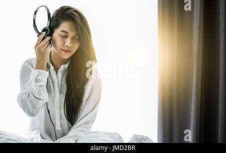 Asiatische Frauen sind Musik mit Kopfhörern hören am Wochenende morgens Relex und Entertainment-Konzept mit Sonnenlicht Stockfoto