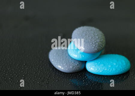 Blaue und graue Kieselsteine mit Wassertropfen in Zen Lebensstil auf schwarzem Hintergrund angeordnet Stockfoto