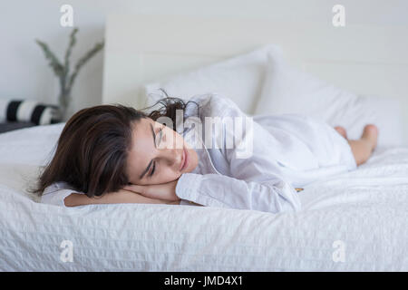 Junge Frau auf Bett trägt ein weißes Hemd. Stockfoto