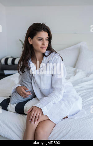 Junge Frau im Bett sitzen und wegsehen. Stockfoto