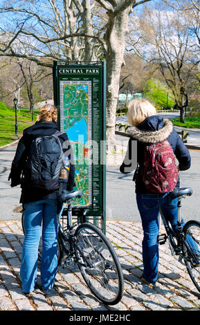 Zwei Frauen auf Fahrrädern im Central Park in New York City, zu stoppen, um zu überprüfen, einen Karte Kiosk für Richtungen Stockfoto