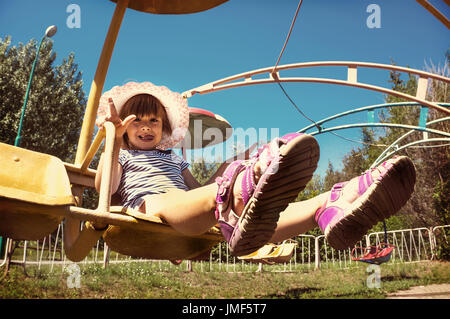 Kleines Mädchen sitzt auf einem drehbaren Karussell im Park. Glücklich und fröhlich Ausdruck. getönte Foto Stockfoto