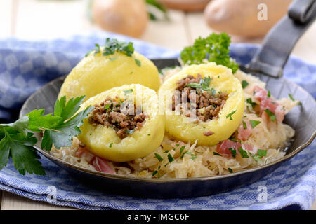 Kartoffelknödel gefüllt mit Hackfleisch, serviert mit Sauerkraut und Speck in einer Eisenpfanne Stockfoto