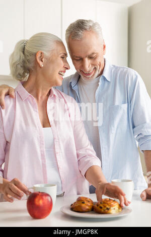 Foto des Lächelns Reifen liebenden paar Familie stehen in der Küche in der Nähe von Apfel und Gebäck. Auf der Suche zur Seite. Stockfoto