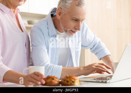 Foto von fröhlichen Reifen liebenden paar Familie stehen in der Küche mit Laptop-Computer. Auf der Suche zur Seite. Stockfoto