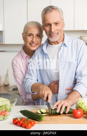 Bild glücklich Reifen liebenden paar Familie stehen in der Küche mit Laptop-Computer und Kochen Salat. Blick in die Kamera. Stockfoto