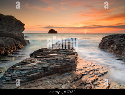 Eine wunderschöne Goldene orange Sonnenuntergang am Trebarwith Strand in Cornwall. Die Felsen des Teilprogramms Schlange heraus ins Meer als die Wellen rund um die Felsen. Stockfoto