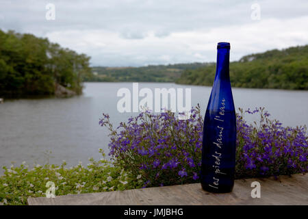 Lac de Guerlédan an der Anse de Sordan, Morbihan, Bretagne: Merlin Les Pieds Dans L'Eau Restaurant mit einer blauen Flasche Wasser im Vordergrund Stockfoto