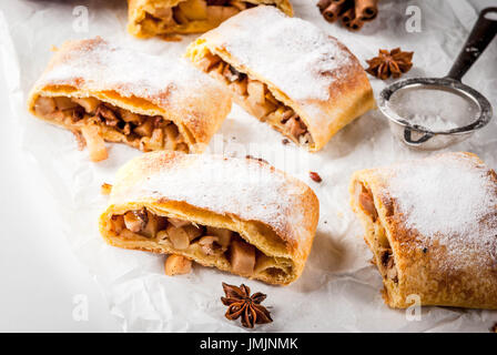 Home Herbst, Sommer, Backen, Blätterteiggebäck. Apfelstrudel mit Nüssen, Rosinen, Zimt und Puderzucker. Auf weißen Marmor Tisch. In Scheiben geschnitten, mit ingredie Stockfoto