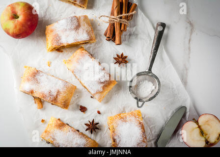 Home Herbst, Sommer, Backen, Blätterteiggebäck. Apfelstrudel mit Nüssen, Rosinen, Zimt und Puderzucker. Auf weißen Marmor Tisch. In Scheiben geschnitten, mit ingredie Stockfoto