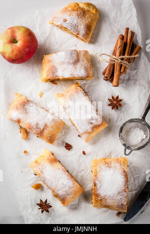 Home Herbst, Sommer, Backen, Blätterteiggebäck. Apfelstrudel mit Nüssen, Rosinen, Zimt und Puderzucker. Auf weißen Marmor Tisch. In Scheiben geschnitten, mit ingredie Stockfoto