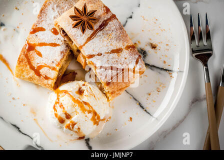 Home Herbst, Sommer, Backen, Blätterteiggebäck. Apfelstrudel mit Nüssen, Rosinen, Zimt und Puderzucker. Auf weißen Marmor Tisch. In Scheiben geschnitten, mit Eis crea Stockfoto