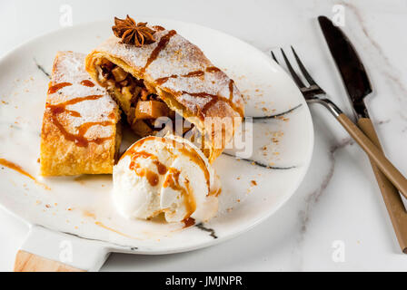 Home Herbst, Sommer, Backen, Blätterteiggebäck. Apfelstrudel mit Nüssen, Rosinen, Zimt und Puderzucker. Auf weißen Marmor Tisch. In Scheiben geschnitten, mit Eis crea Stockfoto