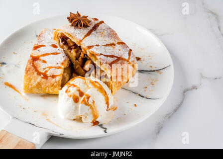 Home Herbst, Sommer, Backen, Blätterteiggebäck. Apfelstrudel mit Nüssen, Rosinen, Zimt und Puderzucker. Auf weißen Marmor Tisch. In Scheiben geschnitten, mit Eis crea Stockfoto