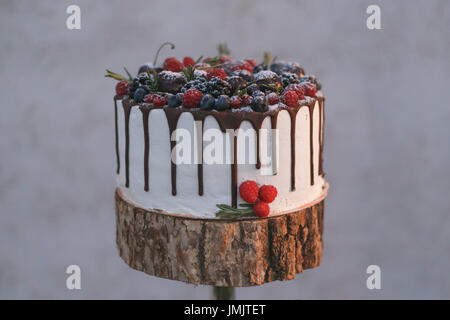 Eine Hochzeitstorte mit Beeren, ausgegossen mit Schokolade auf einem Regal aus Holz Stockfoto