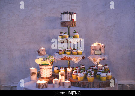Hochzeit Kuchen und Muffins mit Kerzen auf einem Regal Holz Stockfoto