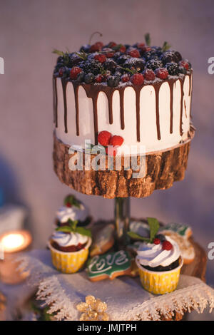 Kuchen und Törtchen mit Beeren auf einem Holzregal im Kerzenschein Stockfoto