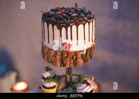 Kuchen und Muffins mit Beeren auf einem Holzregal im Kerzenschein. Stockfoto