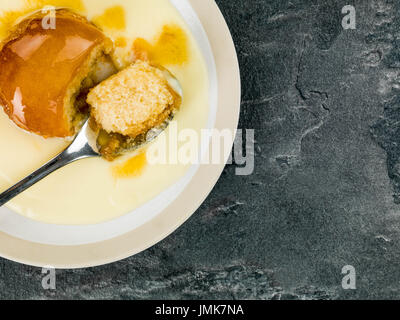 Sirup oder Melasse Sponge Pudding mit Custard gegen eine schwarze texturiert Kachelhintergrund Stockfoto