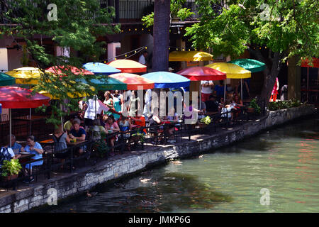 Leute sitzen an den Sonnenschirm beschattet Restaurant Tischen entlang des San Antonio Riverwalk. Stockfoto