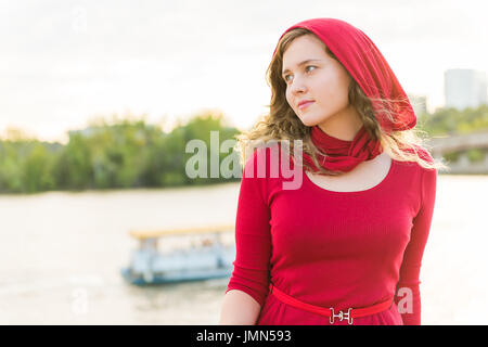 Junge Frau im roten Kleid mit Schal auf dem Kopf sitzen Denken von Potomac River während des Sonnenuntergangs Stockfoto