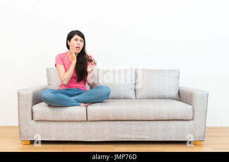 junge schöne Studentin Essen Donut Dessert Gefühl Zahn schmerzhaft auf Sofa mit Blick auf weißem Hintergrund zeigt deprimiert emotionale ich sitzen Stockfoto